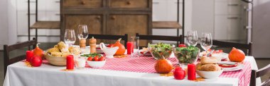 Şükran Günü 'nde salata, bardak, mum, sebze, karabiber değirmeni, mısır, tuz değirmeni ve balkabağı ile panoramik bir resim. 