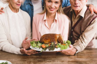 cropped view of smiling family members holding plate with tasty turkey in Thanksgiving day   clipart