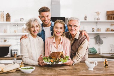 Gülümseyen aile üyeleri Şükran Günü 'nde ellerinde lezzetli hindiyle tabakları tutuyorlar.  
