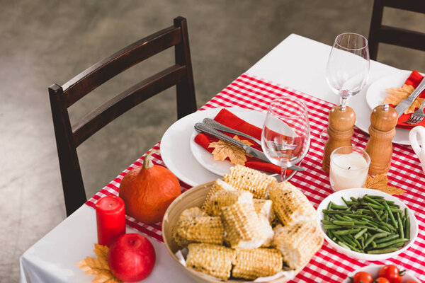 высокий угол обзора стола со спаржей, стаканами, свечами, перцовой мельницей, соляной мельницей, кукурузой, тарелками, столовыми приборами и тыквой в День Благодарения
 