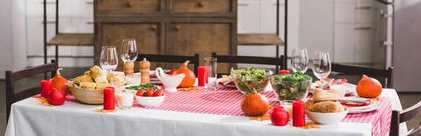 panoramic shot of table with salad, glasses, candles, vegetables, pepper mill, corn, salt mill and pumpkins in Thanksgiving day 