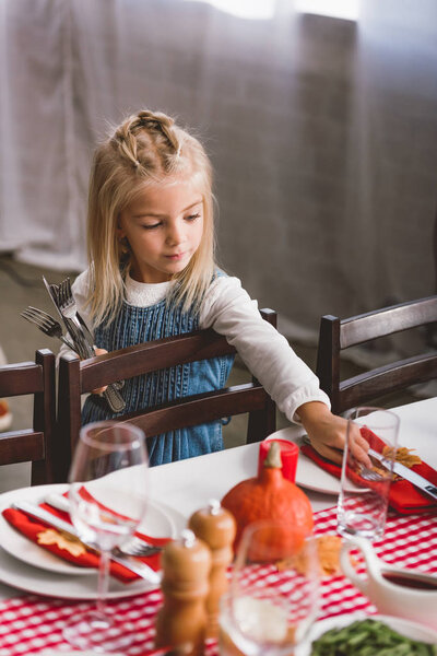 selective focus of cute kid smiling and putting on table cutlery in Thanksgiving day  