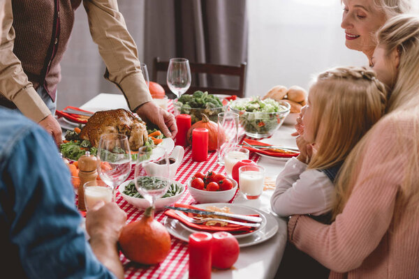 family members sitting at table and grandfather holding plate with turkey in Thanksgiving day      