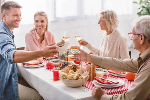 smiling family members sitting at table and clinking with wine glasses in Thanksgiving day   