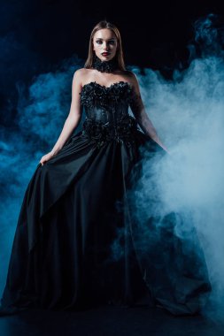 Siyah arka planda siyah gotik kıyafetli, dumanlı korkunç vampir kız.