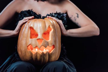 cropped view of girl in black gothic dress holding carved Halloween pumpkin with candles isolated on black clipart