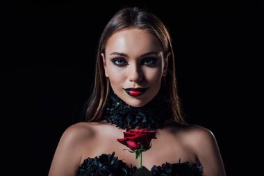 Siyah gotik elbiseli, gülümseyen, korkunç vampir kız elinde siyah bir gül tutuyor.