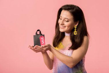 Gülümseyen şık disko kızı elinde alışveriş çantası, üzerinde pembe etiketler var.