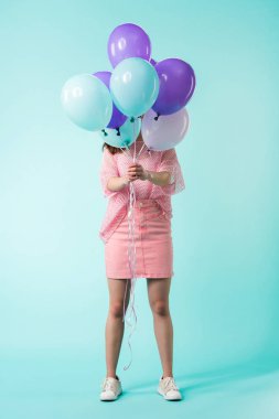 girl in pink outfit holding balloons in front of face on turquoise background clipart