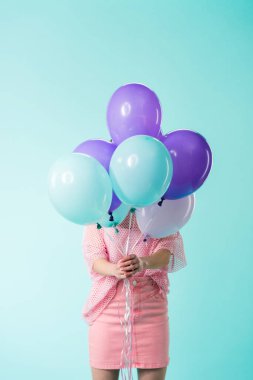 Pembe elbiseli kız yüzün önünde balon tutuyor. Turkuazda izole edilmiş.