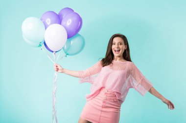 Pembe elbiseli mutlu kız turkuazda izole edilmiş balonlar tutuyor.
