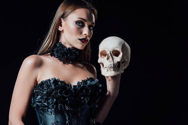 scary vampire girl in black gothic dress holding human skull isolated on black