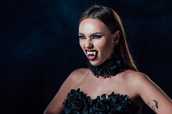 scary vampire girl with fangs in black gothic dress isolated on black