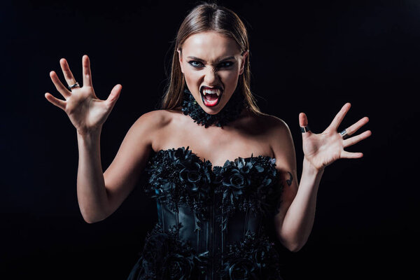 scary vampire girl with fangs in black gothic dress isolated on black