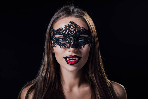 naked scary vampire girl in masquerade mask showing fangs isolated on black