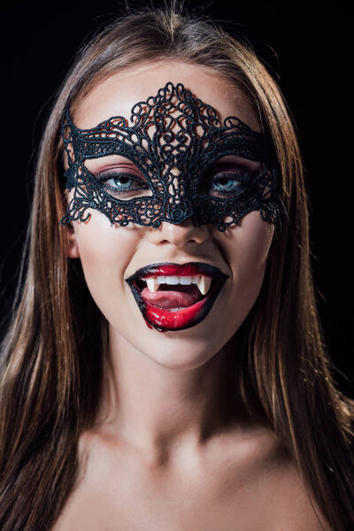 naked scary vampire girl in masquerade mask showing fangs isolated on black