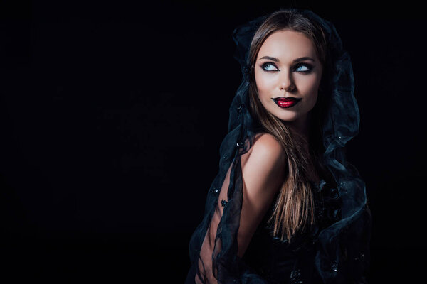 страшная девушка-вампир в черно-готическом платье и вуали, смотрящая в сторону изолированной на черном
