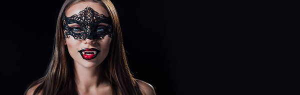 panoramic shot of naked scary vampire girl in masquerade mask showing fangs isolated on black