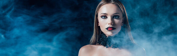 panoramic shot of scary vampire girl in black gothic dress on black background with smoke