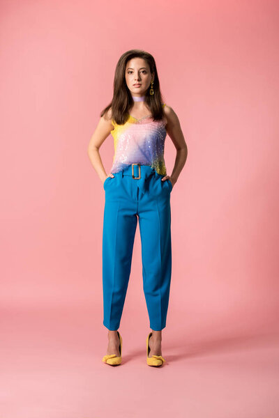 full length view of young stylish disco girl with hands in pockets isolated on pink