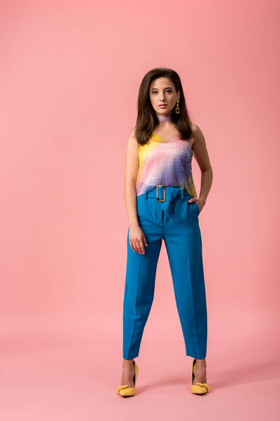 full length view of young stylish disco girl with hand in pocket isolated on pink