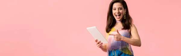 兴奋的年轻时尚迪斯科女孩用手指指向用粉色隔离的数码平板电脑的全景照片 — 图库照片