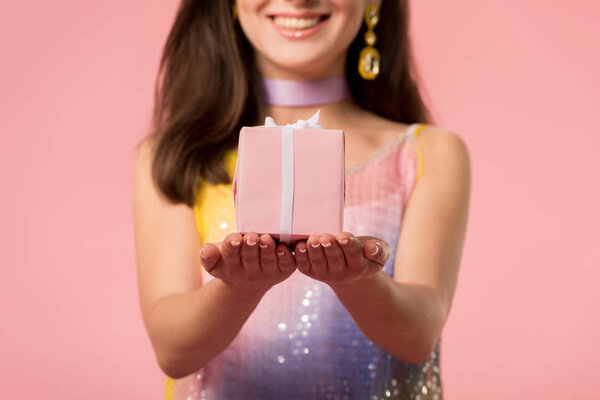 cropped view of happy young stylish disco girl holding gift box isolated on pink