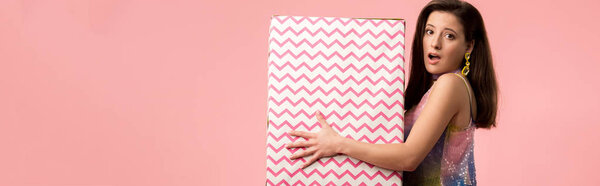 panoramic shot of shocked young stylish disco girl holding huge gift box isolated on pink