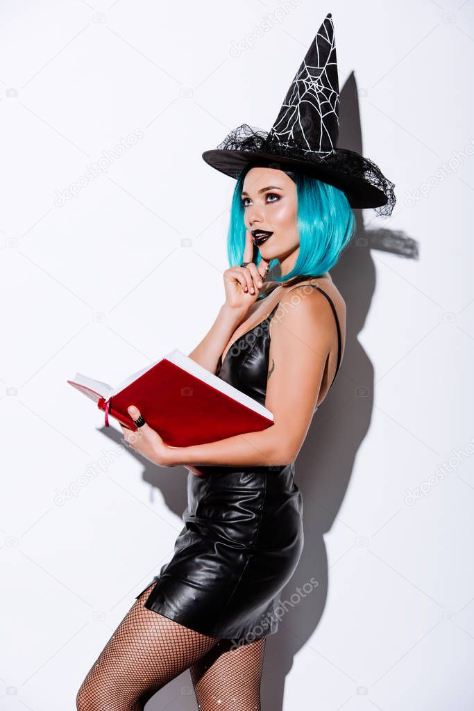 sexy girl in black witch Halloween costume with blue hair holding book on white background