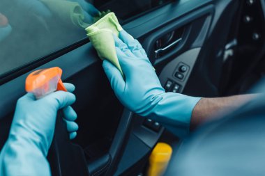 Araba temizleyicisinin araba kapısını temizlerken elinde bez ve sprey şişeyle görüntüsü.