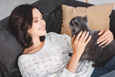 İskoç kedisiyle kanepeye uzanmış mutlu bir kadın.