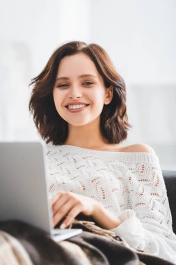 Güzel esmer kız rahat oturma odasındaki kanepede dizüstü bilgisayar kullanıyor.