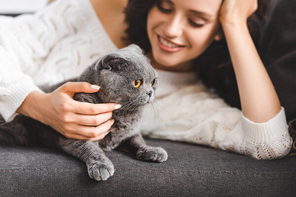 cheerful woman lying on sofa with scottish fold cat  