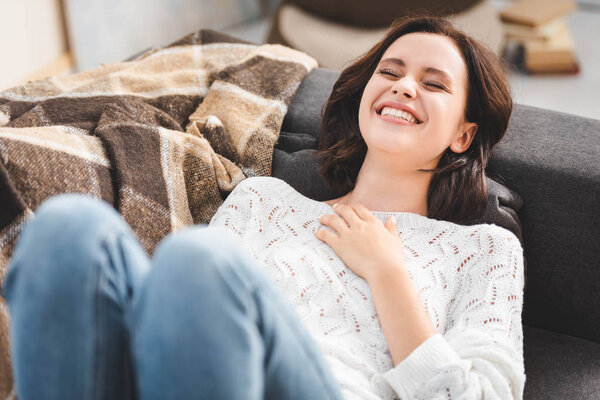 beautiful happy girl laughing and lying on sofa with blanket