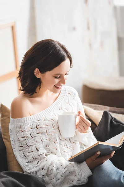 Kanepede Kahve Fincanıyla Kitap Okuyan Neşeli Esmer Kız — Stok fotoğraf