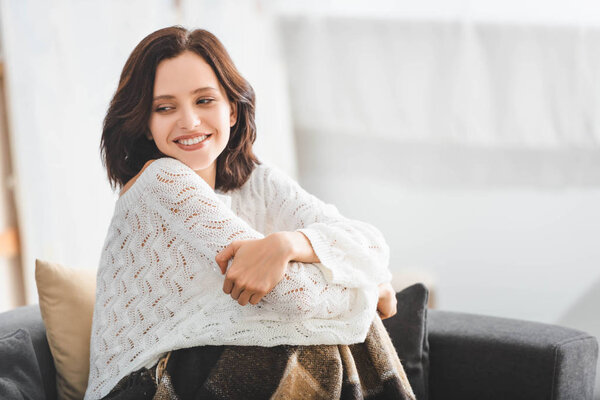 beautiful happy woman with blanket sitting on sofa in cozy living room 