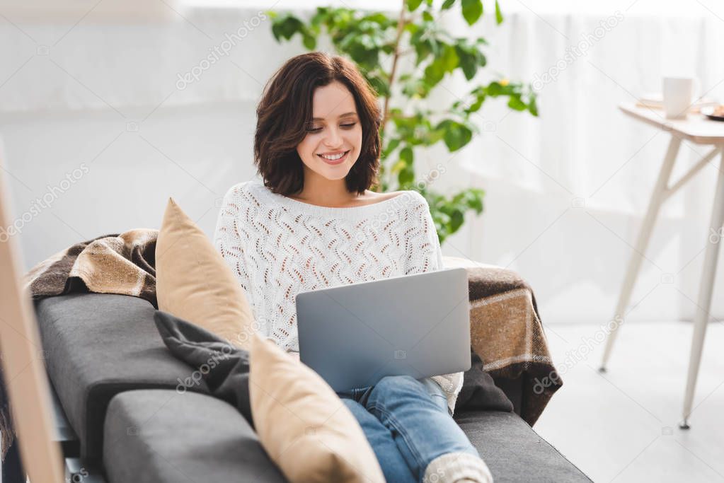 beautiful cheerful girl using laptop on sofa in cozy living room