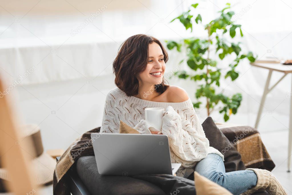 beautiful happy woman with cup of tea using laptop at cozy home