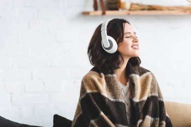 Kapalı gözleri olan mutlu bir kadın kulaklıkla müzik dinliyor.