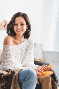 Güzel, mutlu, esmer kız elinde sarı sonbahar yaprakları tutuyor.