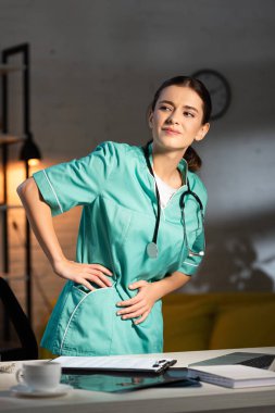 Gece vardiyasında sırtı ağrıyan üniformalı çekici hemşire.