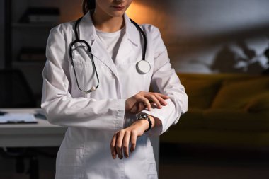 Steteskoplu beyaz önlüklü doktorun gece vardiyasında kol saatine baktığı görüntüler.