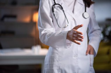 Beyaz önlüklü, steteskoplu, gece vardiyası boyunca uzanan elleri olan doktor görüntüsü.