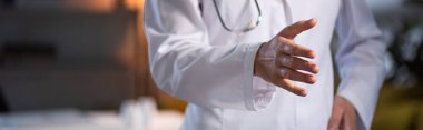 Beyaz önlüklü, steteskoplu, gece vardiyası boyunca uzanan elleri olan doktor görüntüsü.