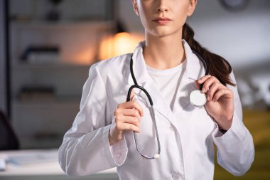 Gece vardiyası boyunca elinde steteskop tutan beyaz önlüklü bir doktor.