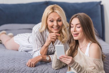 Neşeli anne ve kız akıllı telefona bakarken gülümsüyor.