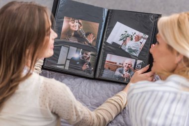 overhead view of mother and daughter talking while lying on bed and looking at photo album clipart