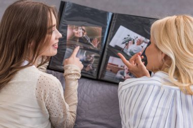 overhead view of mother and daughter talking and pointing with finger at photo album while lying on bed clipart