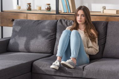 Evdeki kanepede oturmuş kameraya bakan düşünceli bir kız.