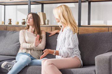 Gücenmiş kız kanepeye oturmuş, annesinin yanında otururken başka tarafa bakıyor.